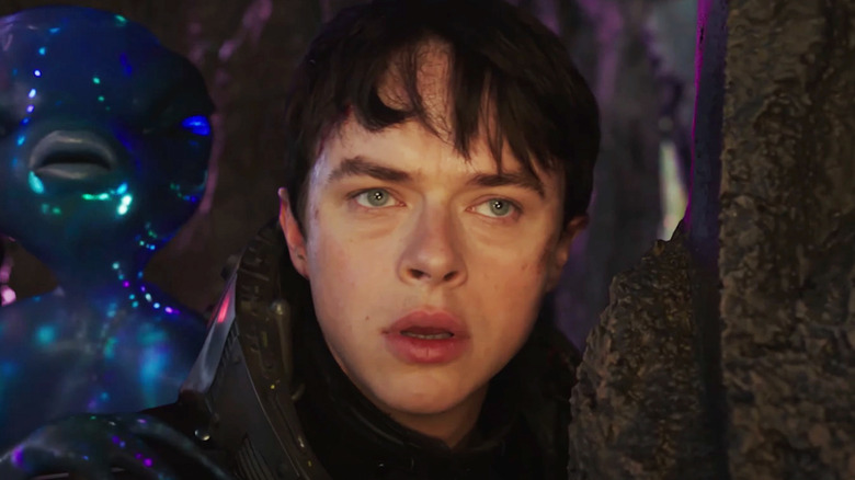 Dane DeHaan's Valerian looks worried standing in front of an alien in Valerian and the City of a Thousand Planets