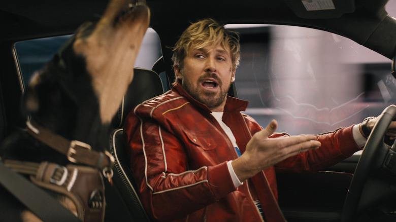 Ryan Gosling as Colt Seavers drives a car with a howling dog riding shotgun in The Fall Guy