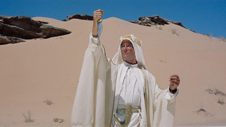 Te Lawrence (Peter O'Toole) berdiri di padang pasir, memegang belati di tangan kanannya dan memandangnya dengan intens di Lawrence of Arabia