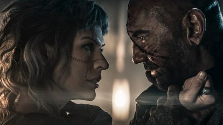 Mila Jovovich's Gray holding a knife to Dave Bautista's throat as Boyce from In the Lost Lands