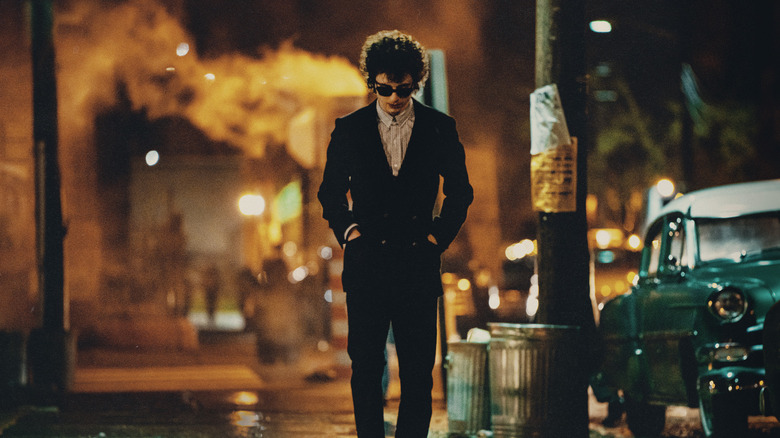 Bob Dylan wears sunglasses at night and walks down the street in A Complete Unknown