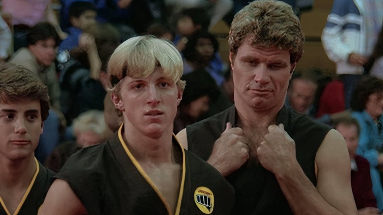 John Kreese grabs his collar while standing next to Johnny Lawrence in The Karate Kid