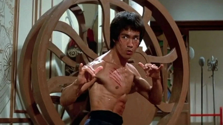 Bruce Lee como Lee sem camisa e em pé defensivamente em Enter the Dragon