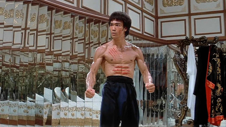 Bruce Lee como Lee em pé na frente de um monte de espelhos em Enter the Dragon