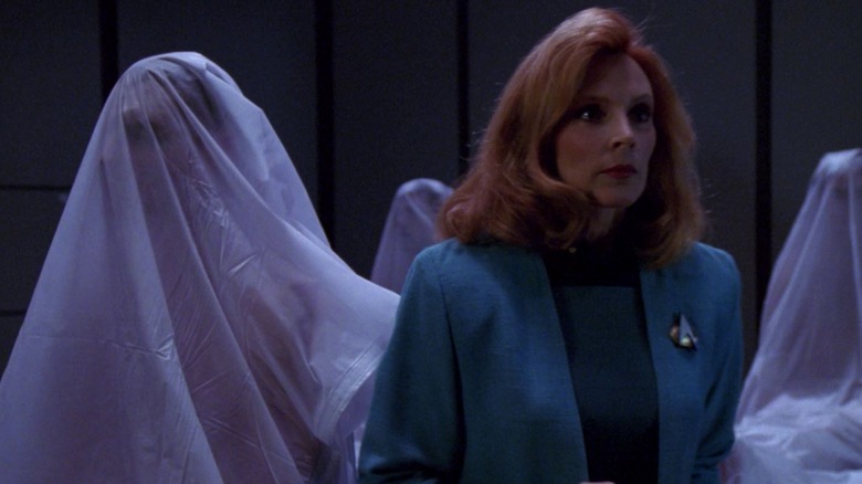 Dr. Crusher standing among sitting-up corpses