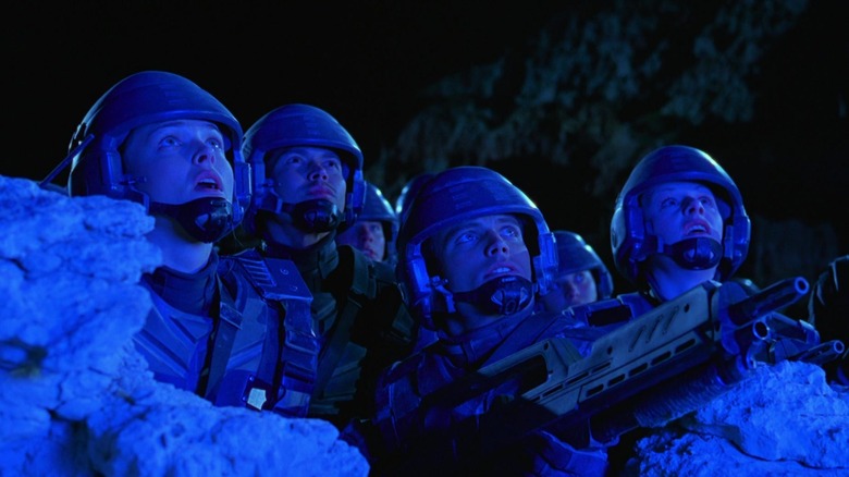 Four of the Starship Troops, in a blue glow, wearing a combat helmet, the war looks in the heaven.