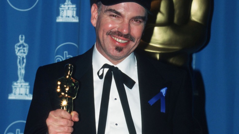 Billy Bob Thornton wearing a baseball cap and a blue ribbon, holding up his Oscar