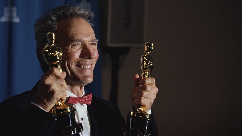 A grinning Clint Eastwood holding up two Oscars