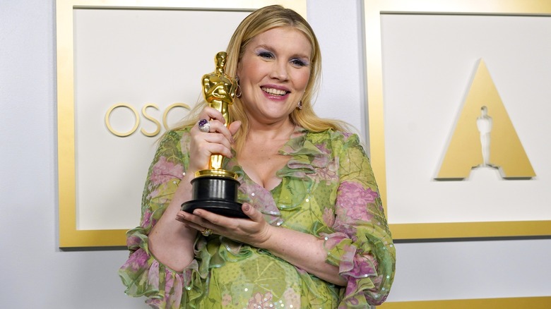 Emerald Fennell holding her Oscar backstage, supporting it at the base