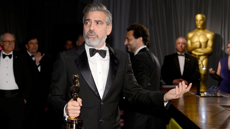 George Clooney holding an Oscar backstage, mid-shrug