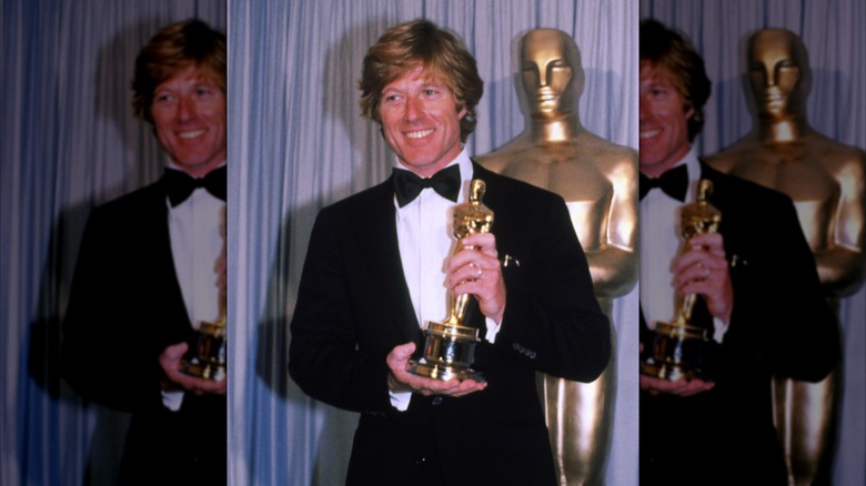 Robert Redford holding his Oscar backstage, supporting it at the base