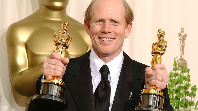 Ron Howard holding two Oscars in front of an Oscar statue