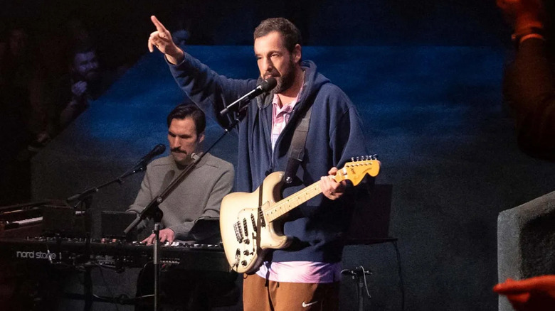 Adam Sandler tocando guitarra e apontando para cima em Love You