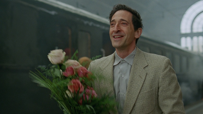 László Tóth holds some flowers and smiles at the train station in The Brutalist