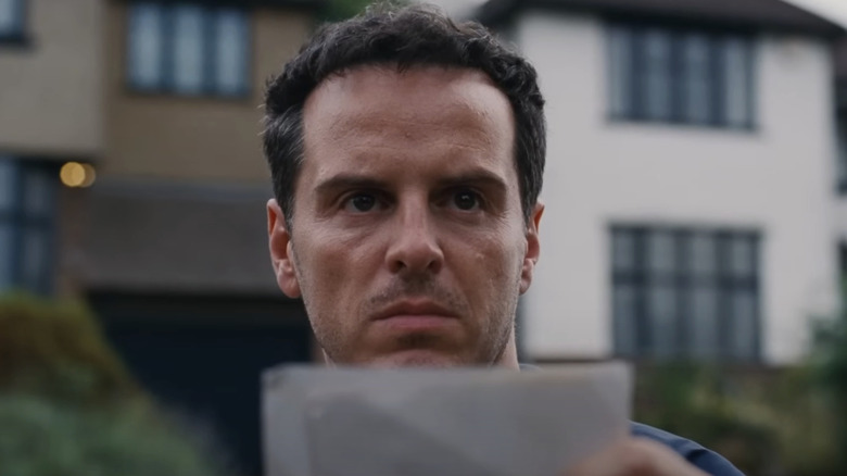 Andrew Scott's Adam holds up a small piece of paper as he looks over the top of it and into the distance in All of Us Strangers