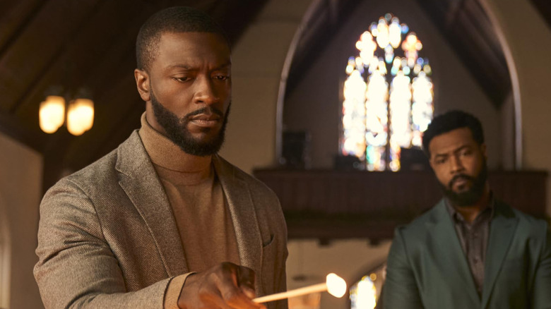 Aldis Hodge as Alex Cross lights a candle while Isaiah Mustafa as John Sampson looks on in Cross