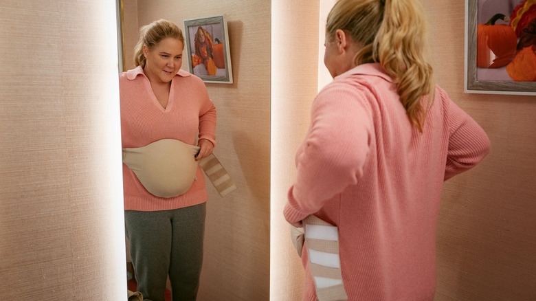 Amy Schumer's Lainy Newton looks at herself in the mirror while wearing a fake baby bump in Kinda Pregnant