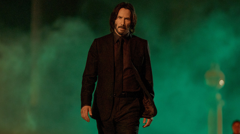 Keanu Reeves as John Wick walking through green mist in John Wick Chapter 4