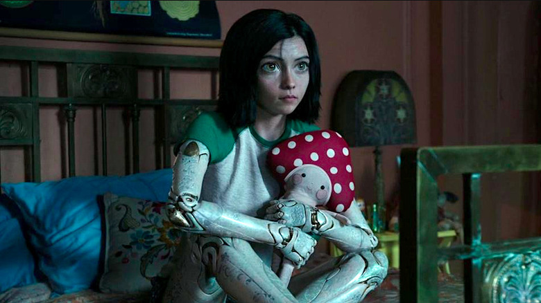 Rosa Salazar sits on the bed while holding a stuffed mushroom in Alita: Battle Angel