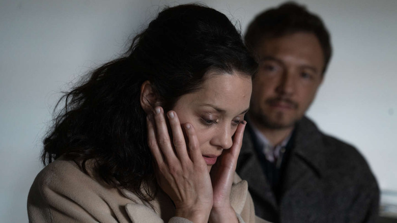 marion cotillard looking down with her cheeks in her hands standing in front of a man in the movie brother and sister