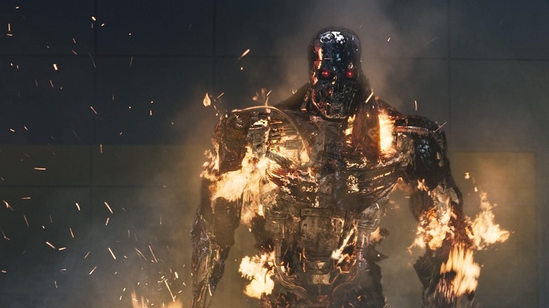 A Terminator robot covered in flames, recovering from a blast to the chest.