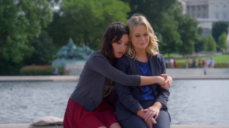 Aubrey Plaza hugging Amy Poehler by a large pond in Parks and Recreation