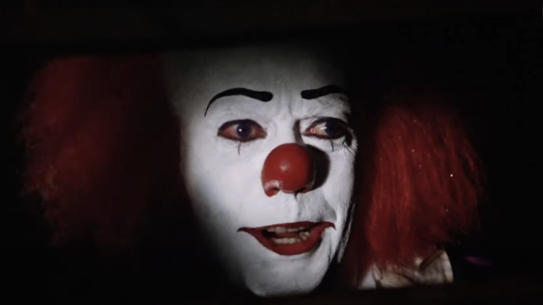 Tim Curry's Pennywise peers out of a sewer in It