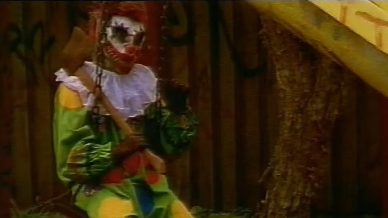 A nasty clown creature sits on a swing in a stigisher