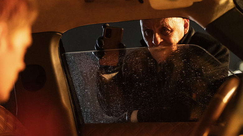 Anthony Hopkins' William holds up a cell phone outside an open window of a vehicle occupied by Bill Skarsgård's Eddie in Locked