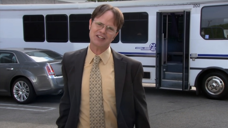 Rainn Wilson's Dwight Shrute stands in front of a bus in The Office