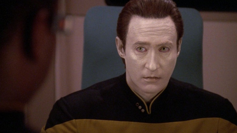 Data, looking at someone intently, sitting in a chair, on Star Trek: The Next Generation.