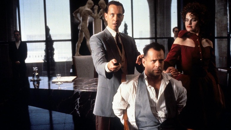 Hudson Hawk tied to a chair, while Darwin and Minerva Mayflower stand smugly over him