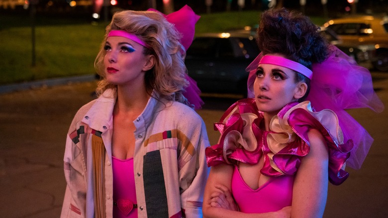 Debbie (Betty Gilpin) and Ruth (Allison Brie) in a parking lot in frilly pink wrestling outfits on GLOW