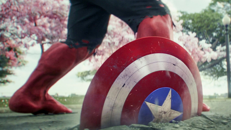 Captain America's shield buried in the ground, with the feet of the red Hulk in the background, in Captain America: the brave new world