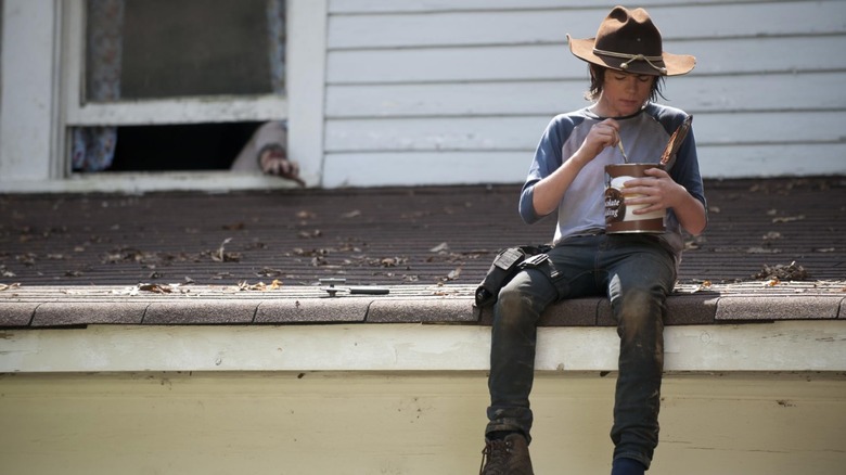 Chandler Riggs' Carl eats chocolate pudding from a big container while sitting on a roof in The Walking Dead