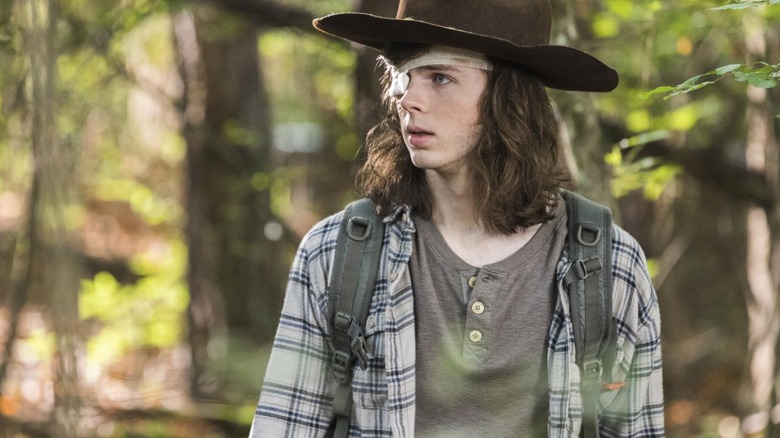 Chandler Riggs' Carl, with an eye patch and big hat, walks through the woods in The Walking Dead