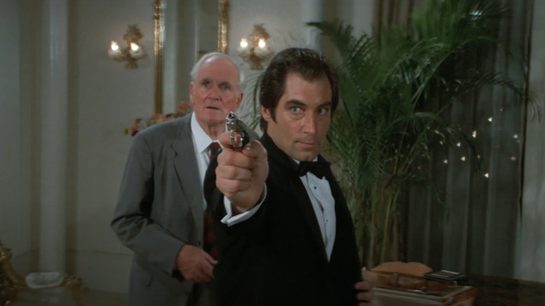 Timothy Dalton membidik sebagai James Bond, di depan Desmond Llewelyn sebagai Q, dalam License to Kill