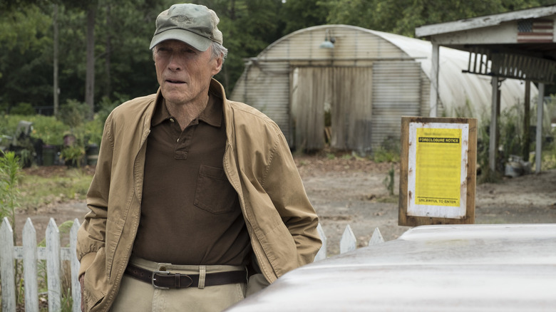 Clint Eastwood as Earl Stone wearing a baseball cap and standing on the side of a truck in the film 