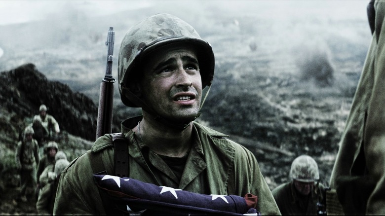 Um soldado segurando uma bandeira americana dobrada no campo de batalha de Iwo Jima