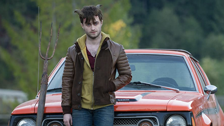 Daniel Radcliffe leaning against a car with a pitchfork