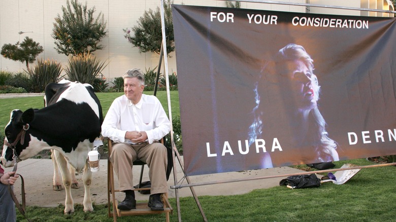 David Lynch sitting on a chair between a cow and a For Your Consideration banner promoting Laura Dern