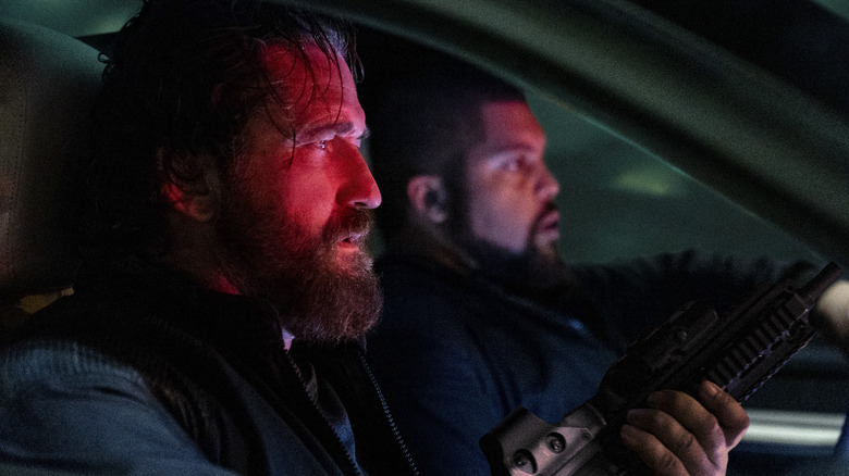 Big Nick and Donnie in the front seat of a car, bathed in red light and holding guns in Den of Thieves 2: Pantera