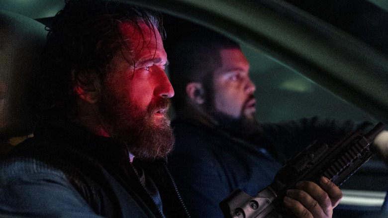 Big Nick y Donnie se sientan en el asiento delantero de un auto, con sus caras bañadas en luz roja, en Den of Thieves 2: Pantera