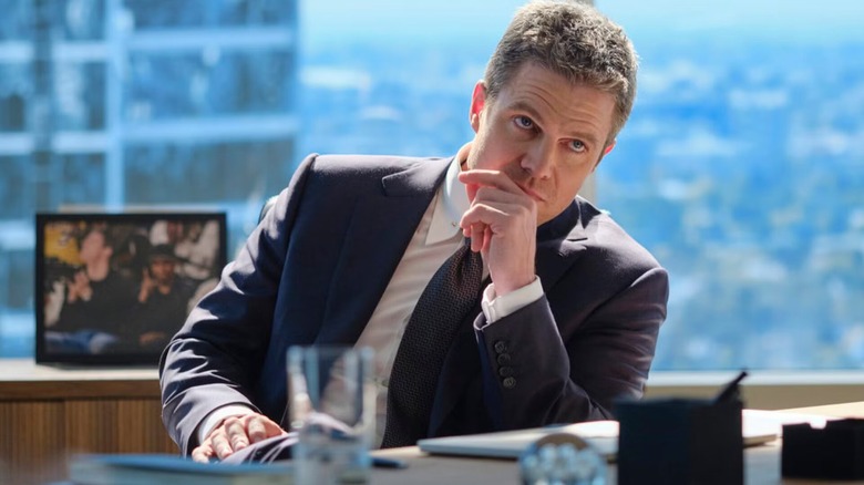 Ted Black sitting at his desk in front of a photo of him and Denzel Washington on Suits LA