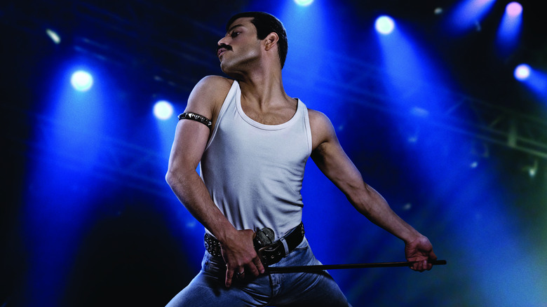 Rami Malek as Freddie Mercury strutting on stage in his tank top with a mic stand in Bohemian Rhapsody