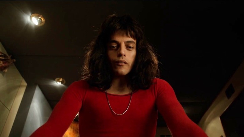 Rami Malek as Freddie Mercury looking down with his long hair in a red shirt in Bohemian Rhapsody