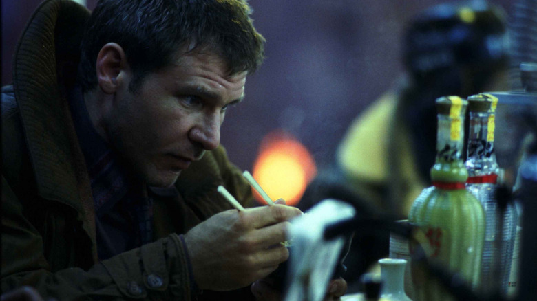 Rick Deckard, sitting at an outdoor foot mart, enjoying a meal with chopsticks in Blade Runner.