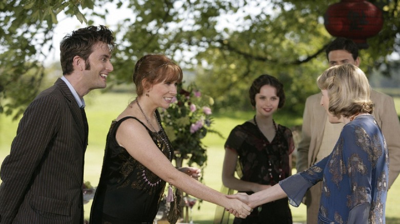 The Doctor (David Tennant) and Donna Noble (Catherine Tate) smile, and Donna shakes the hand of Agatha Christie (Fenella Woolgar) at an outdoor garden party while others look on happily on Doctor Who