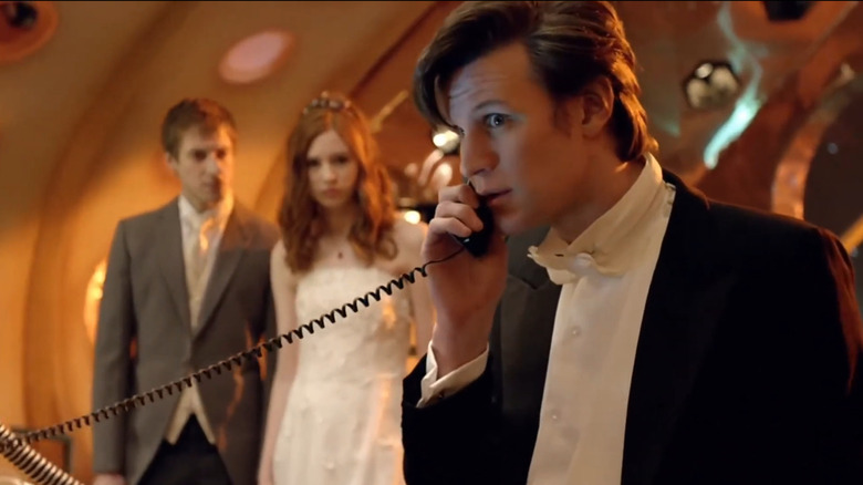 Doctor Who, o 11º médico recebendo um telefonema perto de Rory e Amy