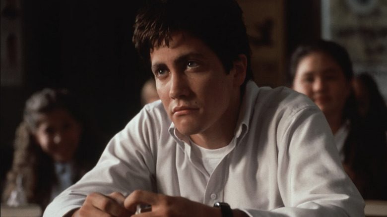 Donnie Darko in a white button up school uniform sitting at his desk looking up